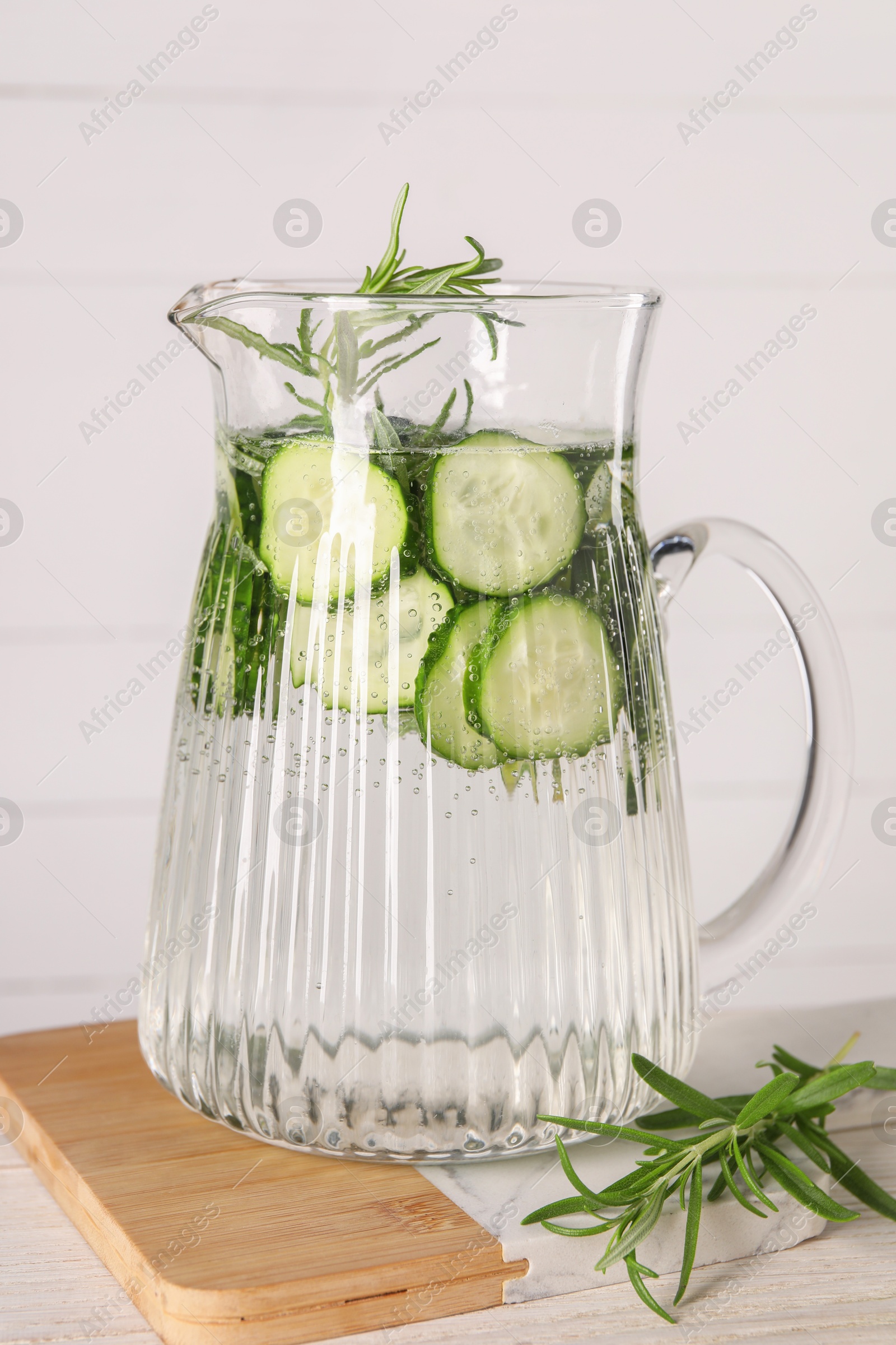 Photo of Refreshing cucumber water with rosemary in jug on light wooden table, closeup