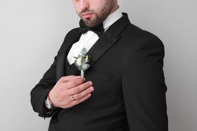 Groom with boutonniere on light grey background, closeup. Wedding accessory