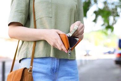 Woman holding purse with banknotes outdoors, closeup