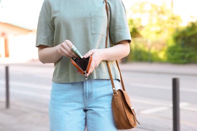 Woman holding purse with banknotes outdoors, closeup