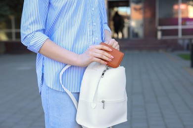 Woman putting purse into bag outdoors, closeup. Space for text