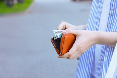 Woman holding purse with banknotes outdoors, closeup. Space for text