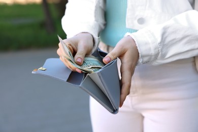 Photo of Woman holding purse with banknotes outdoors, closeup