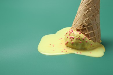 Melted ice cream in wafer cone on pale green background, closeup. Space for text