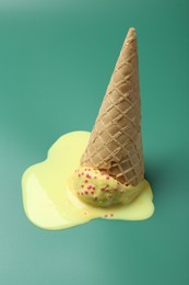 Melted ice cream in wafer cone on pale green background