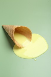 Melted ice cream and wafer cone on light green background