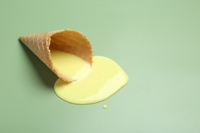 Melted ice cream and wafer cone on light green background. Space for text