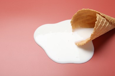 Photo of Melted ice cream and wafer cone on pale pink background, closeup. Space for text