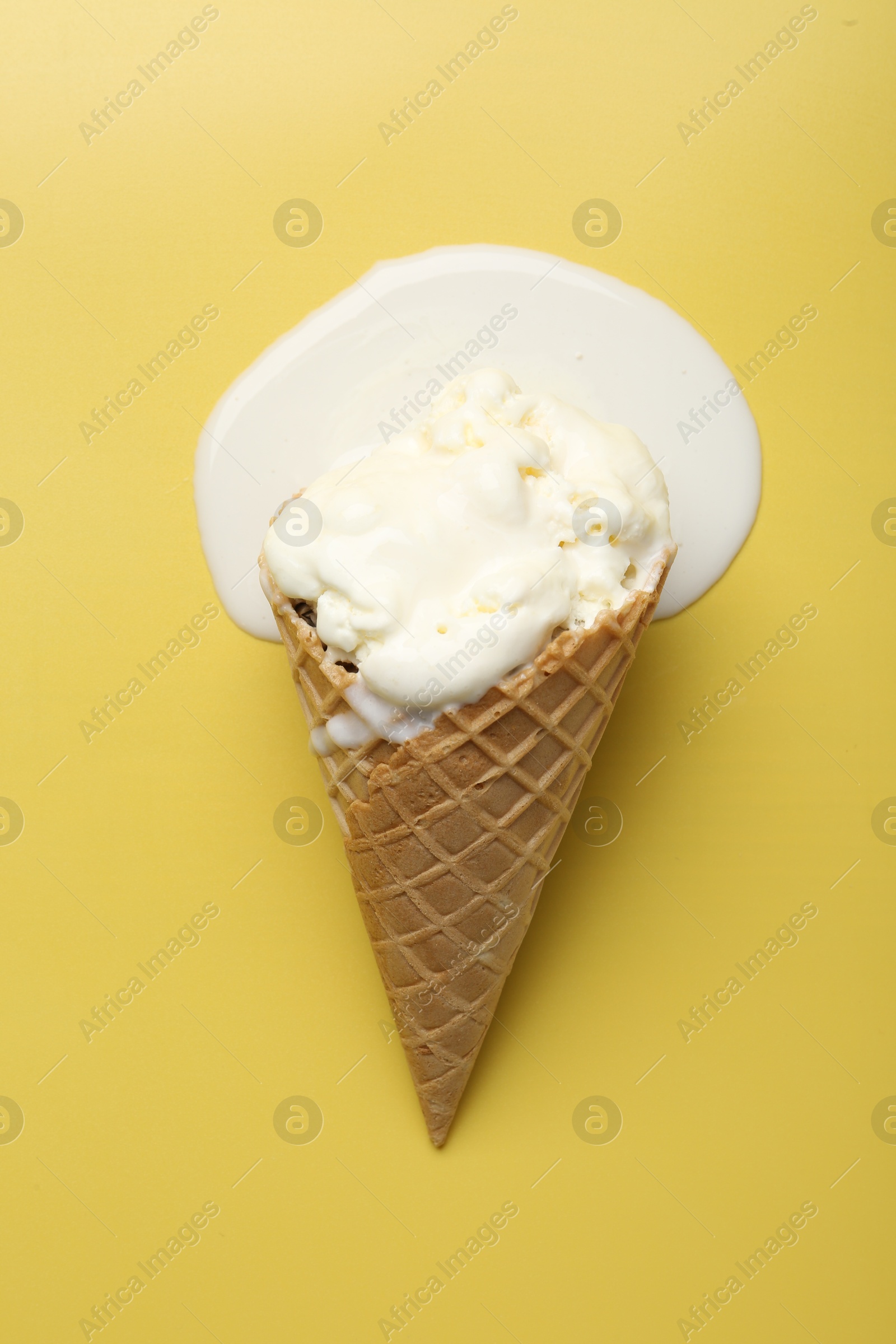 Photo of Melted ice cream in wafer cone on yellow background, top view