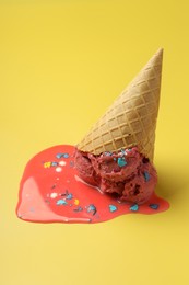 Melted ice cream in wafer cone on yellow background