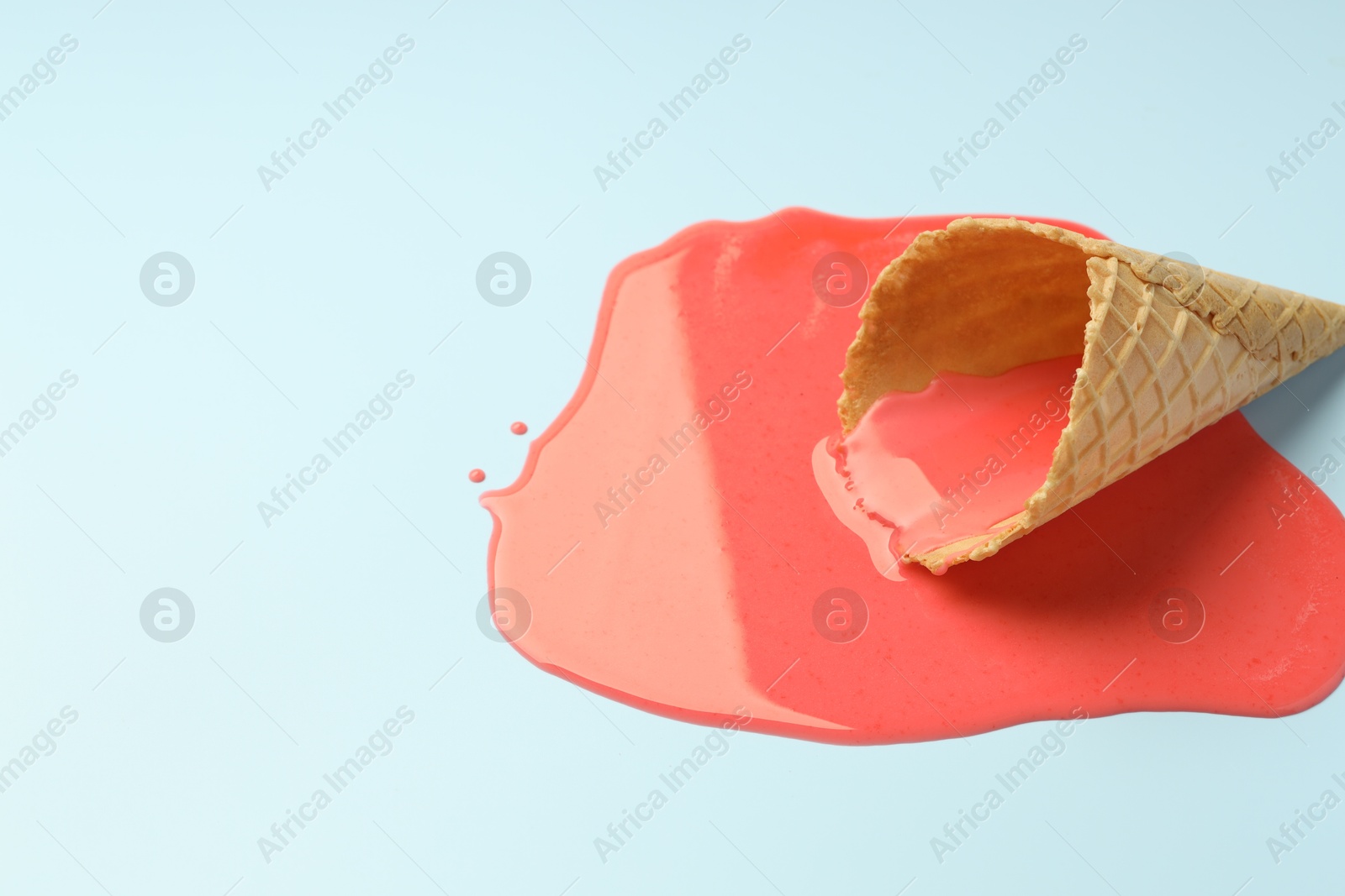 Photo of Melted ice cream and wafer cone on light blue background. Space for text