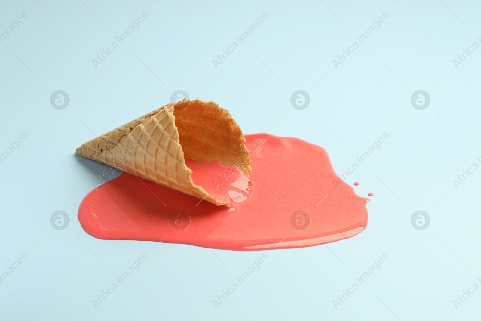 Photo of Melted ice cream and wafer cone on light blue background