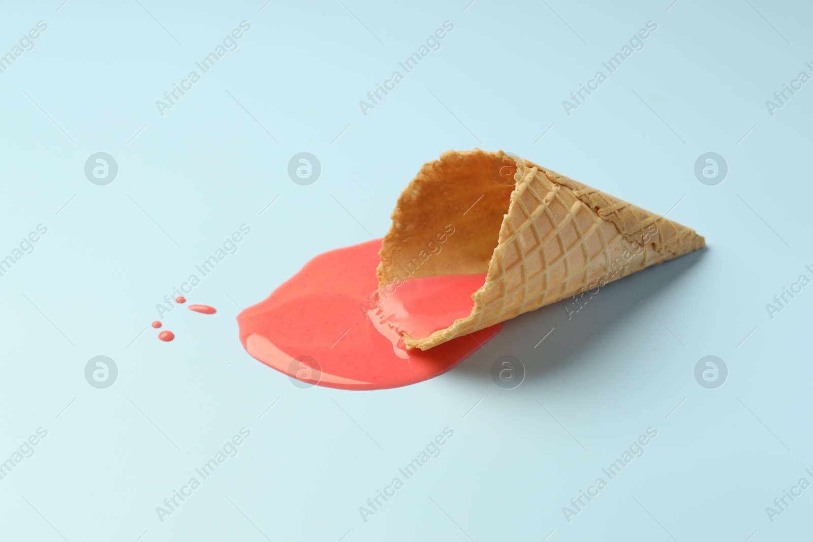 Photo of Melted ice cream and wafer cone on light blue background. Space for text