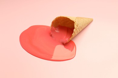 Melted ice cream and wafer cone on light pink background