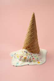 Photo of Melted ice cream in wafer cone on light pink background