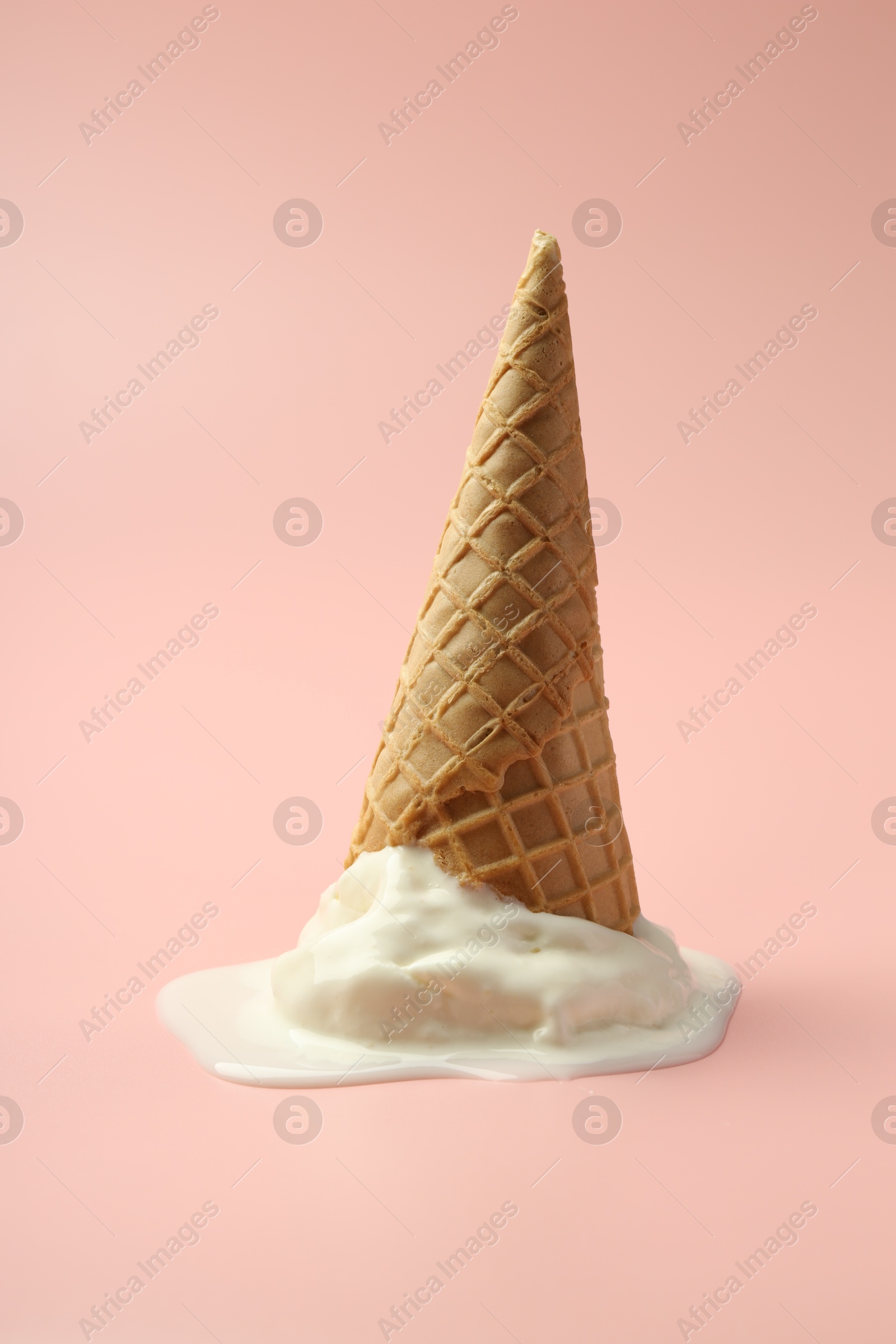 Photo of Melted ice cream in wafer cone on light pink background