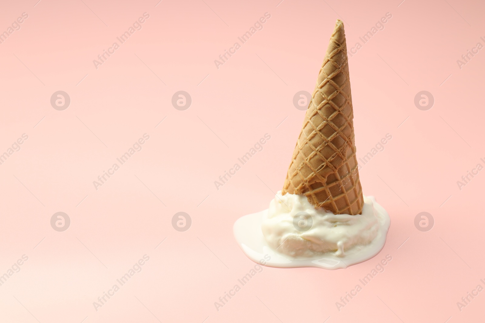 Photo of Melted ice cream in wafer cone on light pink background. Space for text