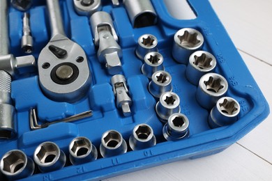 Photo of Auto mechanic's tools in plastic box on white wooden table, closeup