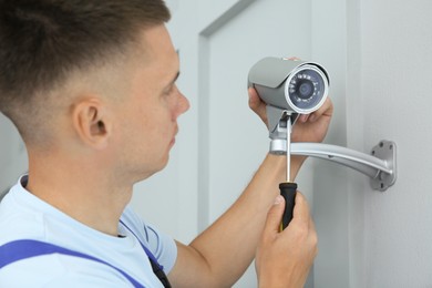 Technician with screwdriver installing CCTV camera on wall indoors