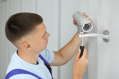 Photo of Technician with screwdriver installing CCTV camera on wall indoors