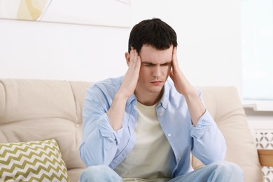 Photo of Man suffering from headache on sofa at home