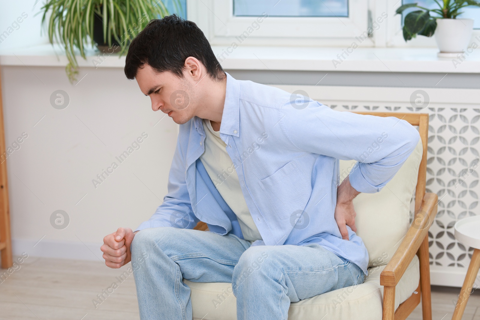 Photo of Man suffering from back pain in armchair indoors