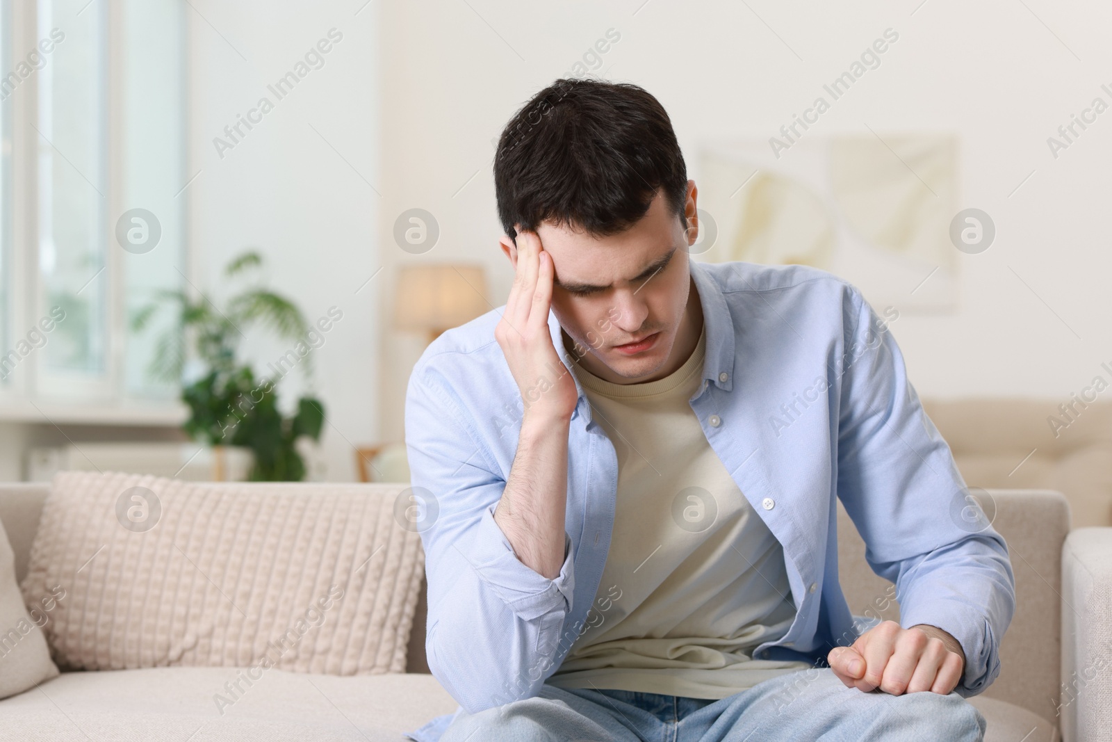 Photo of Man suffering from headache on sofa at home