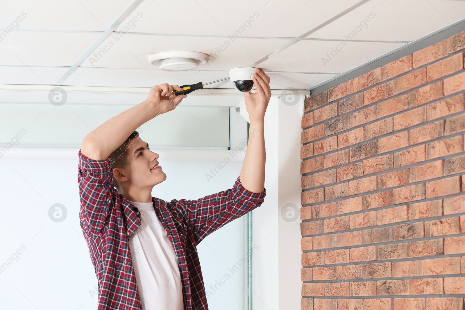 Photo of Technician with screwdriver installing CCTV camera on ceiling indoors