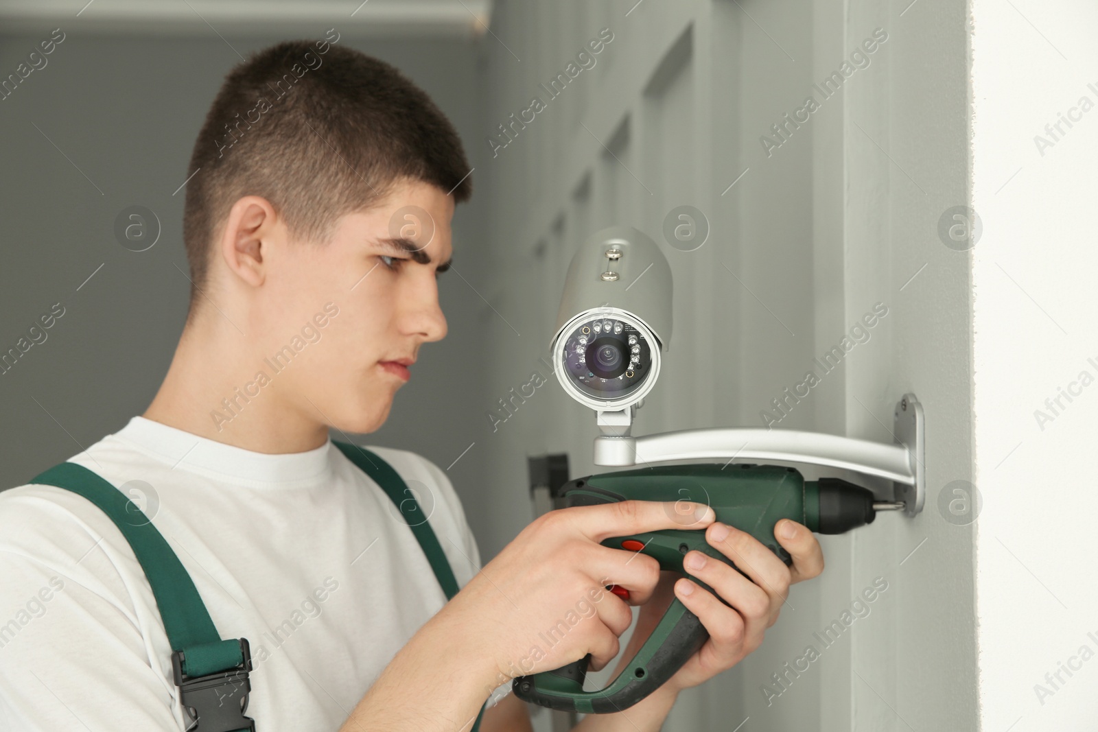 Photo of Technician with cordless electric screwdriver installing CCTV camera on wall indoors