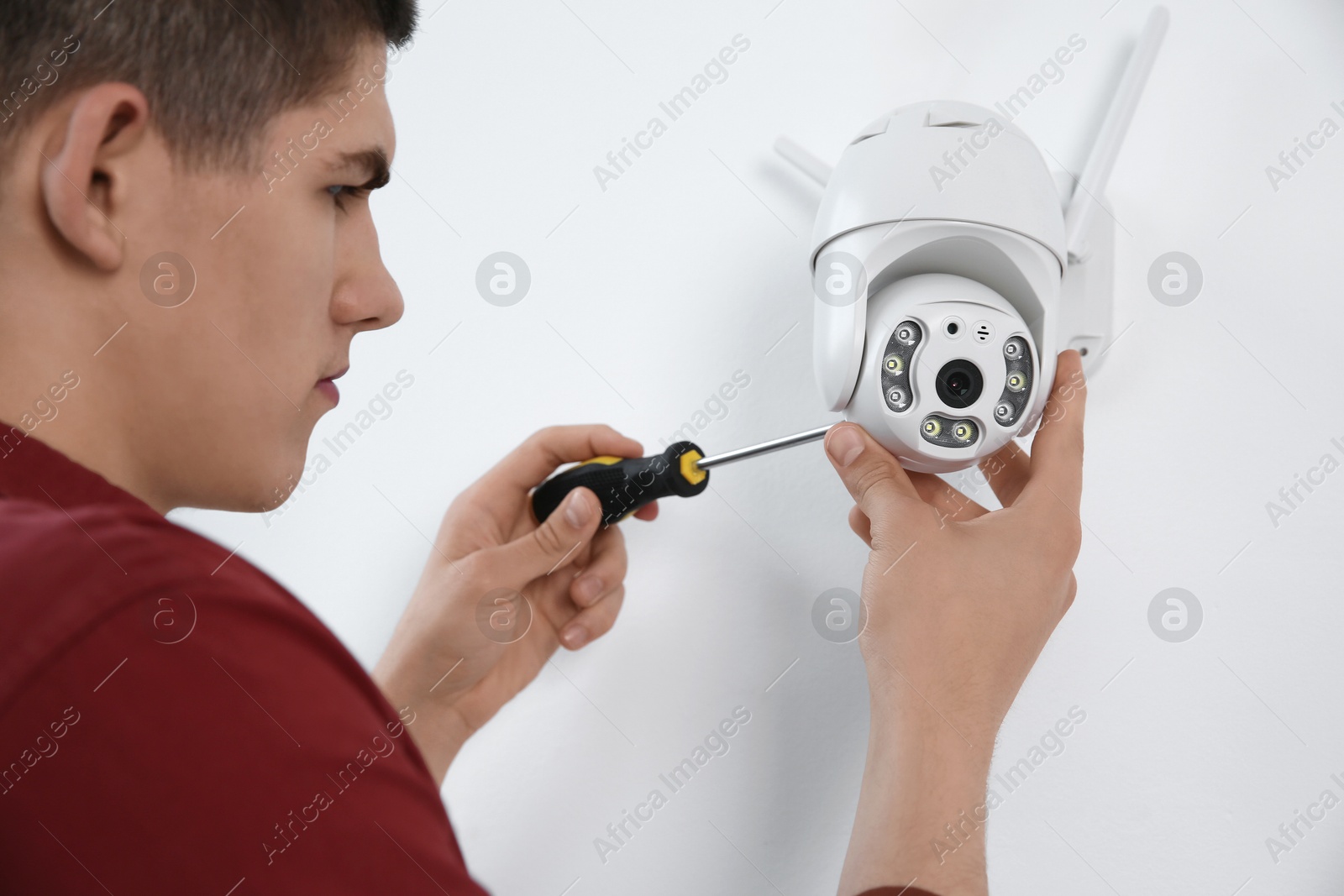 Photo of Technician with screwdriver installing CCTV camera on wall indoors