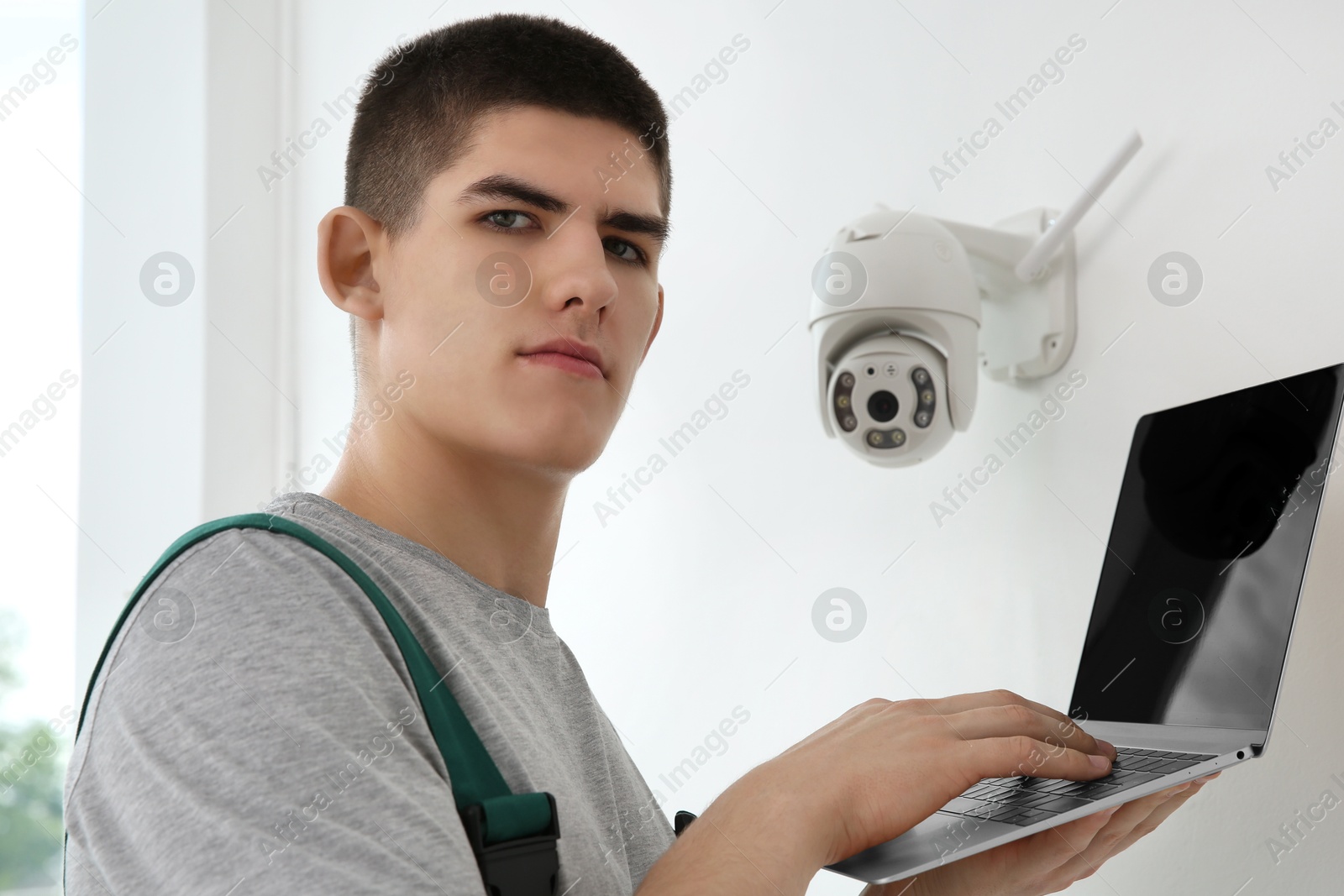 Photo of Technician with laptop installing CCTV camera on wall indoors