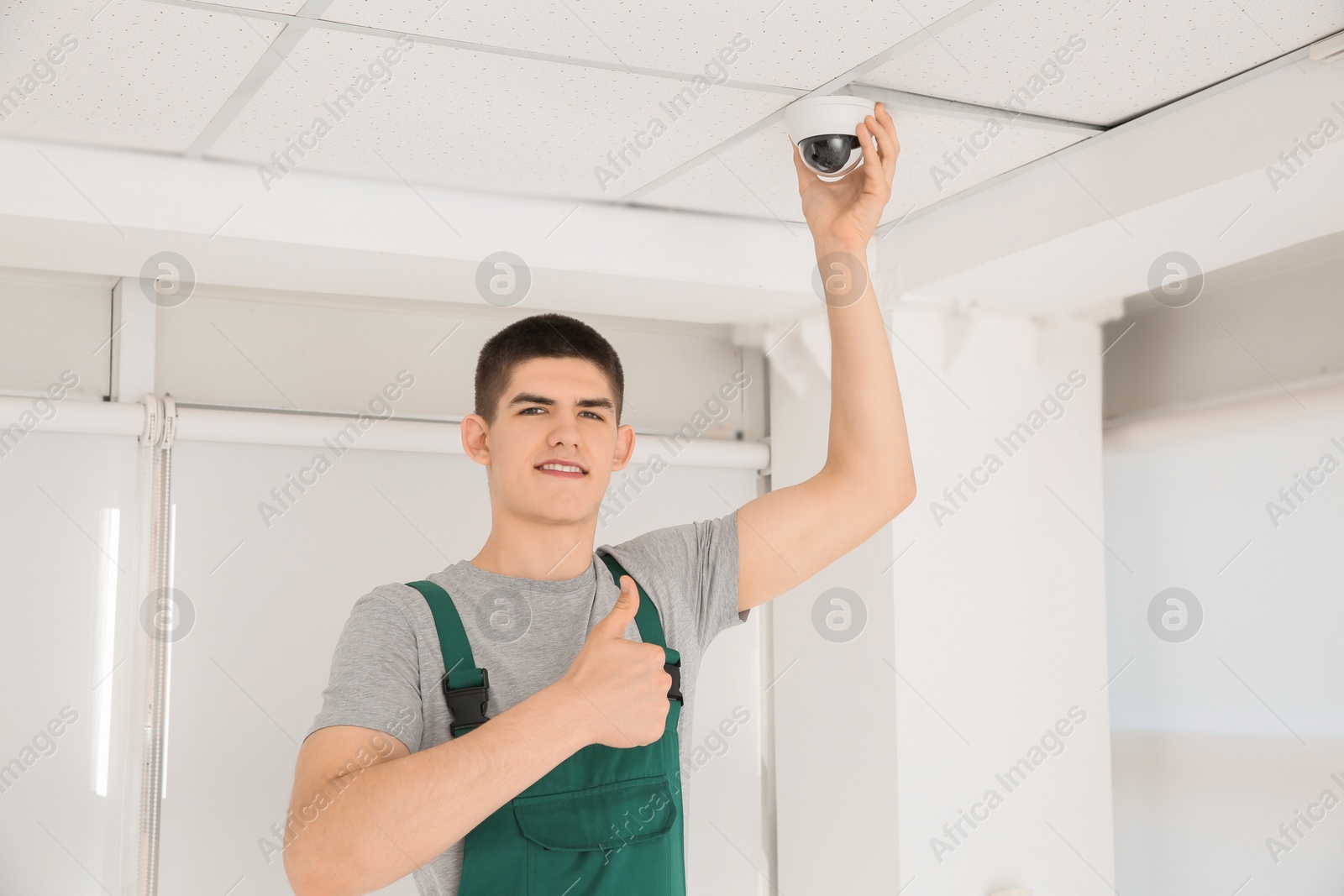 Photo of Technician showing thumbs up while installing CCTV camera on ceiling indoors