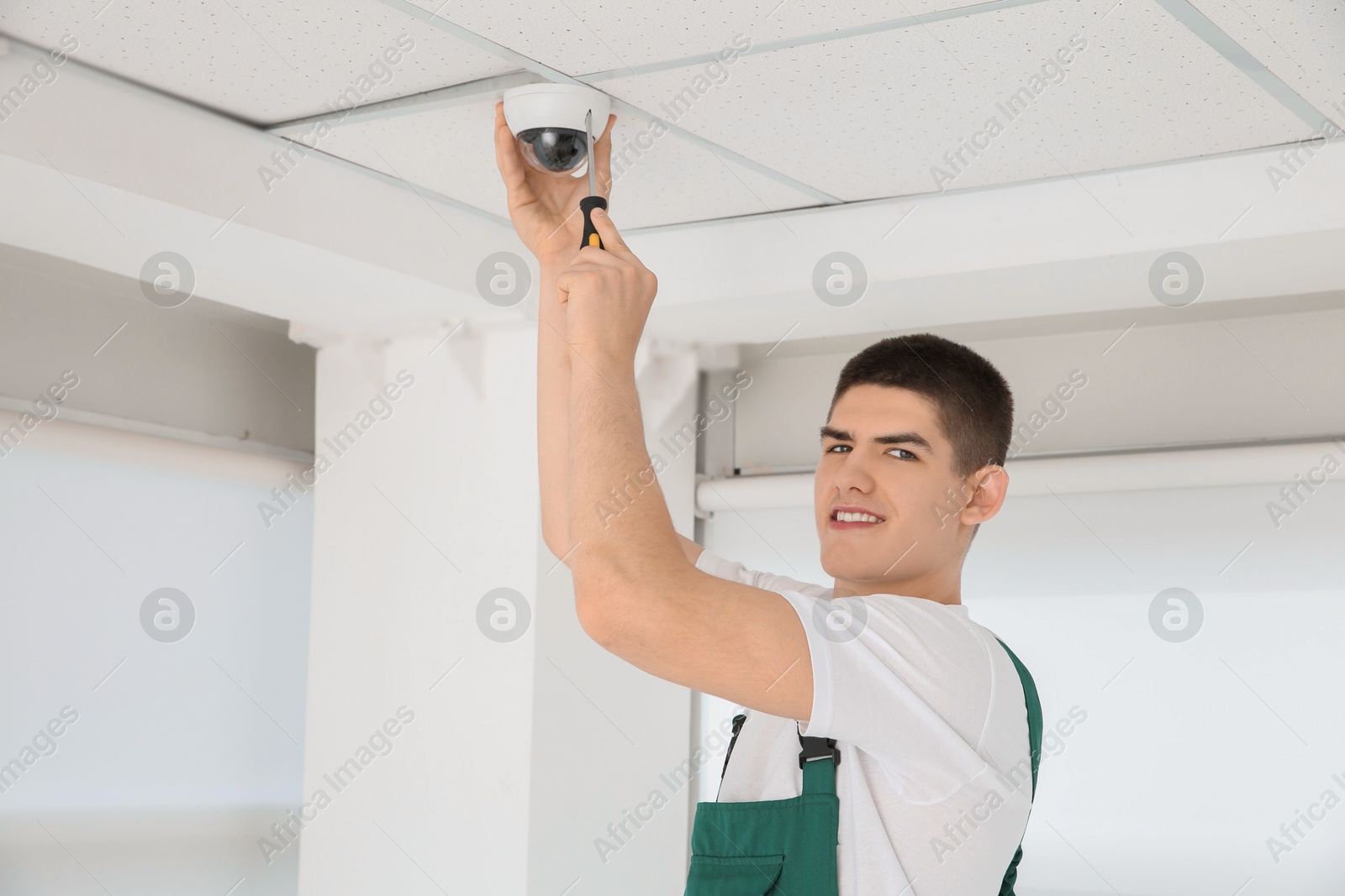 Photo of Technician with screwdriver installing CCTV camera on ceiling indoors