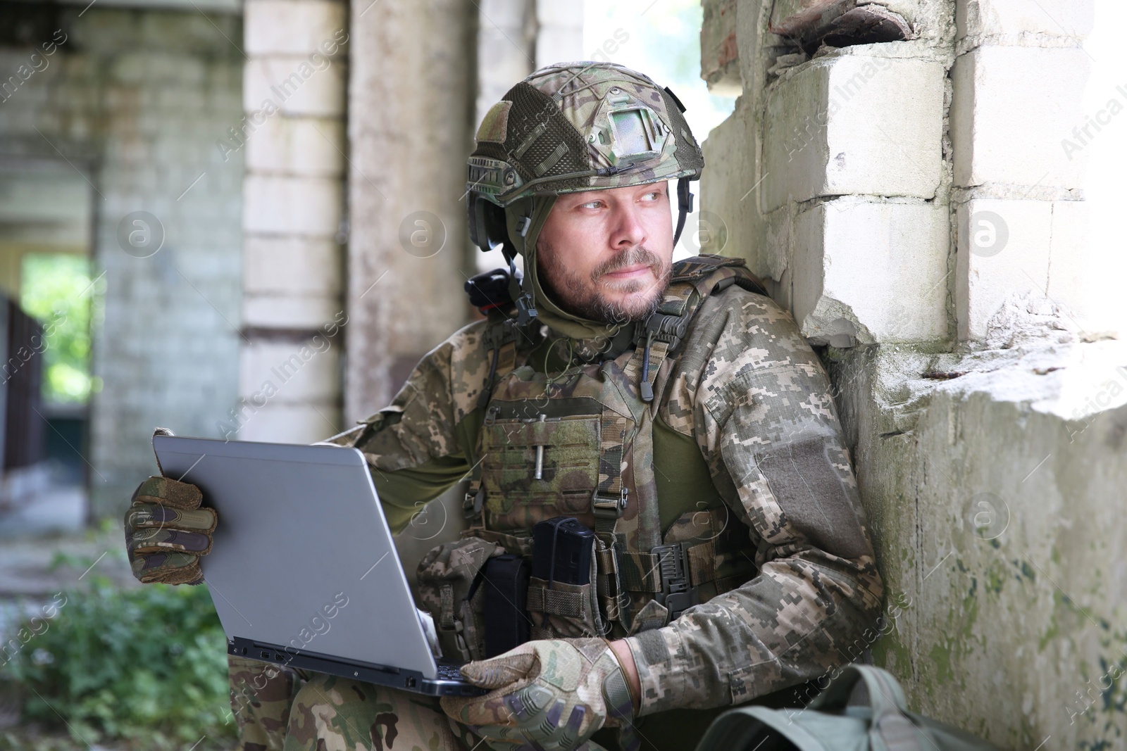 Photo of Military mission. Soldier in uniform using laptop inside abandoned building