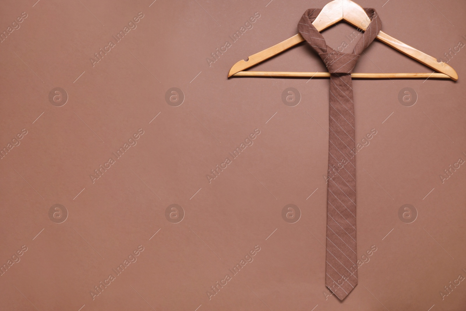 Photo of Hanger with striped necktie on brown background. Space for text