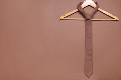 Photo of Hanger with striped necktie on brown background. Space for text