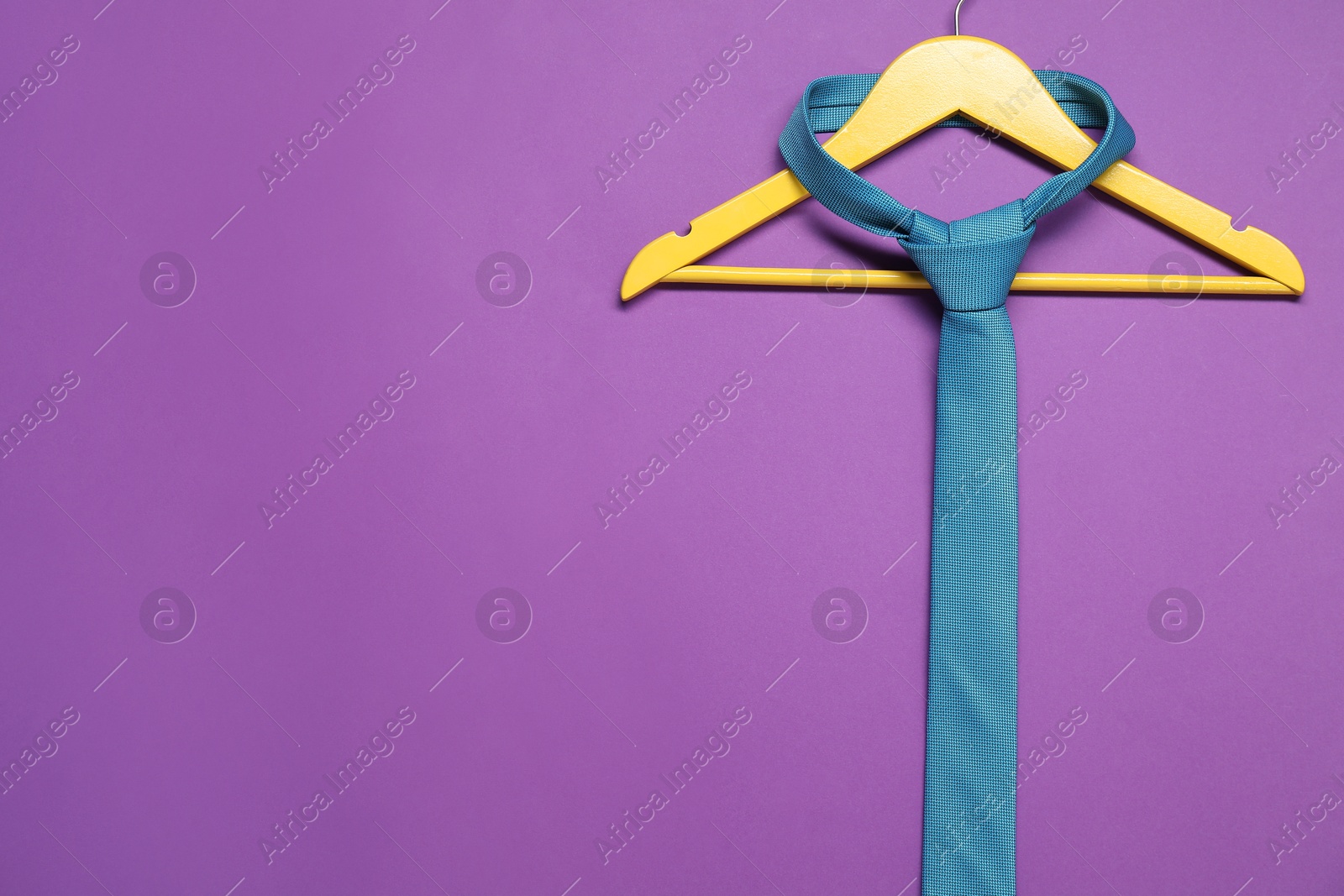 Photo of Hanger with necktie on purple background. Space for text