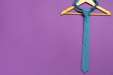 Hanger with necktie on purple background. Space for text