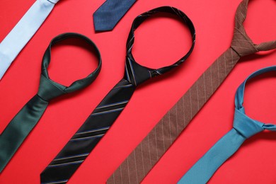 Different neckties on red background, flat lay