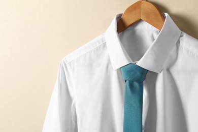 Photo of Hanger with shirt and necktie on beige background