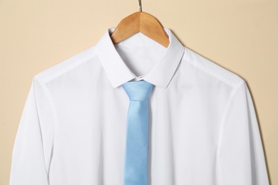Hanger with shirt and necktie on beige background