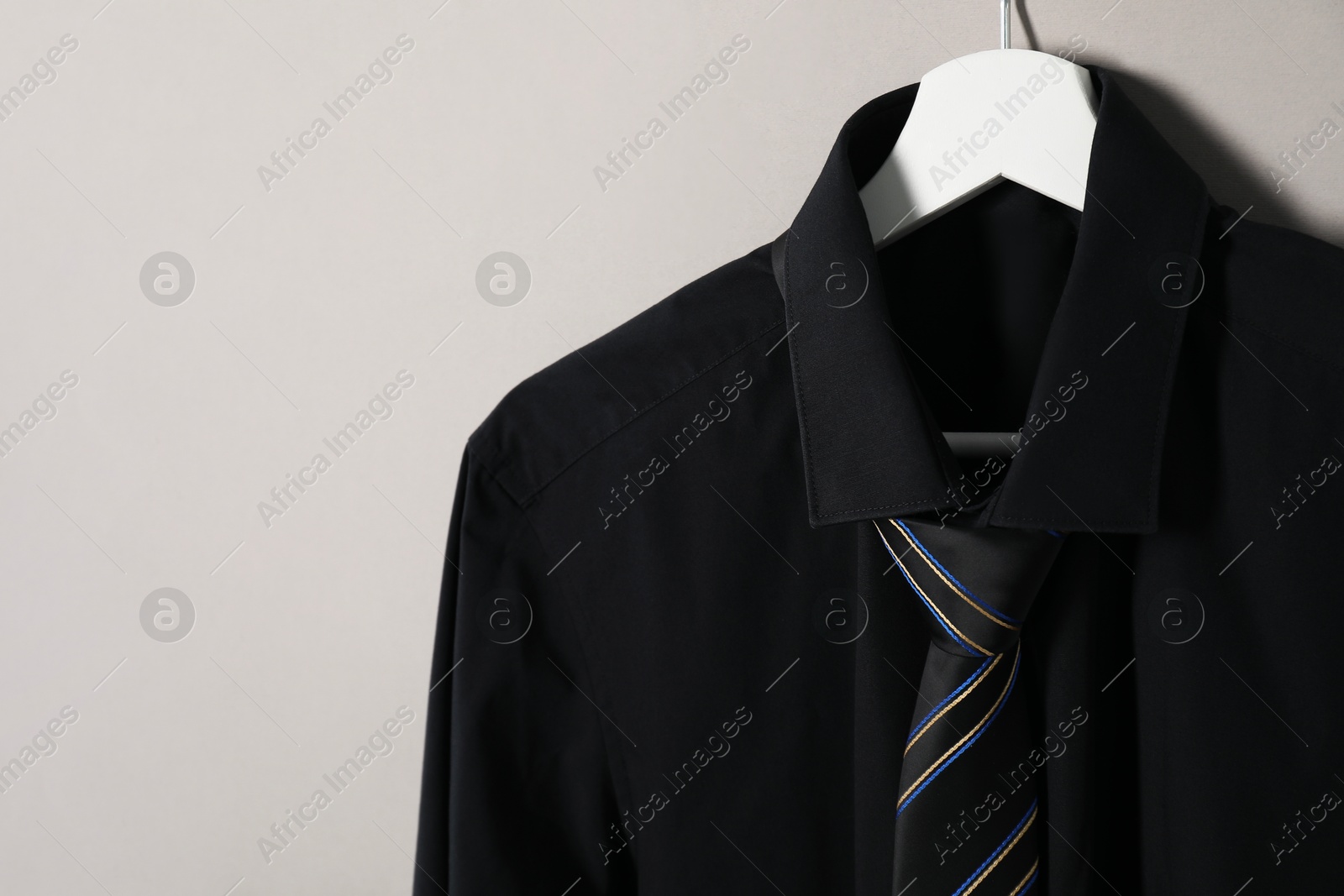 Photo of Hanger with shirt and striped necktie on light background. Space for text