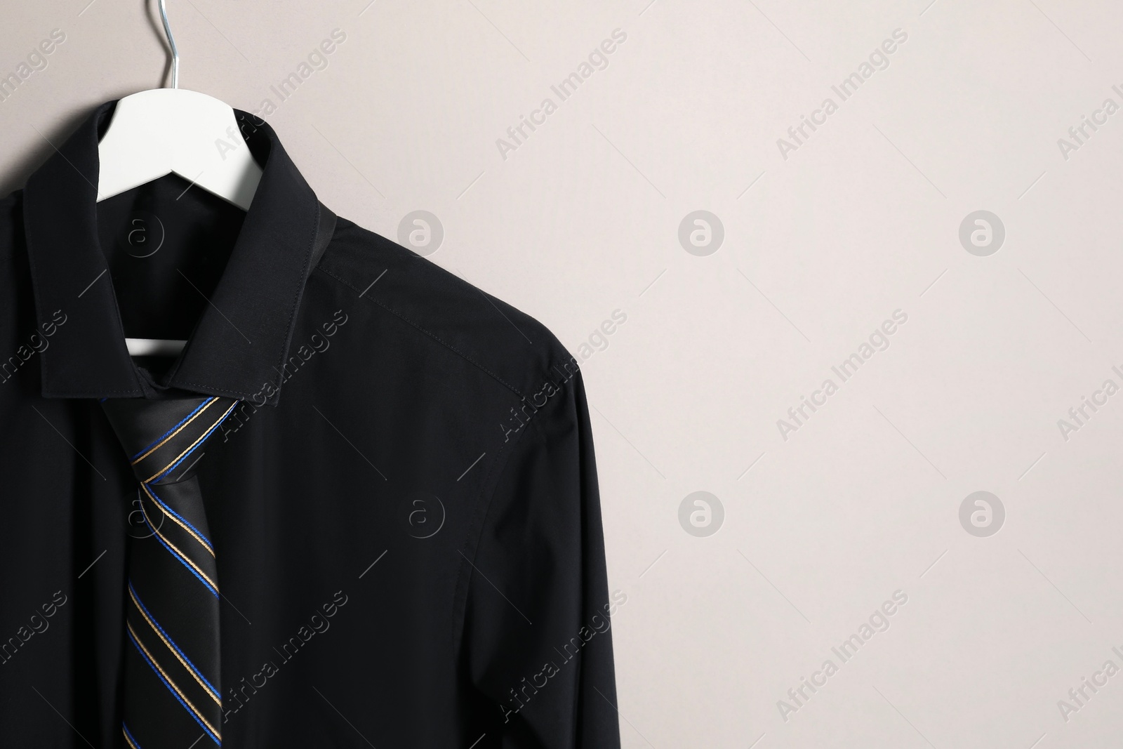 Photo of Hanger with shirt and striped necktie on light background. Space for text