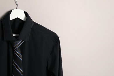 Hanger with shirt and striped necktie on light background. Space for text