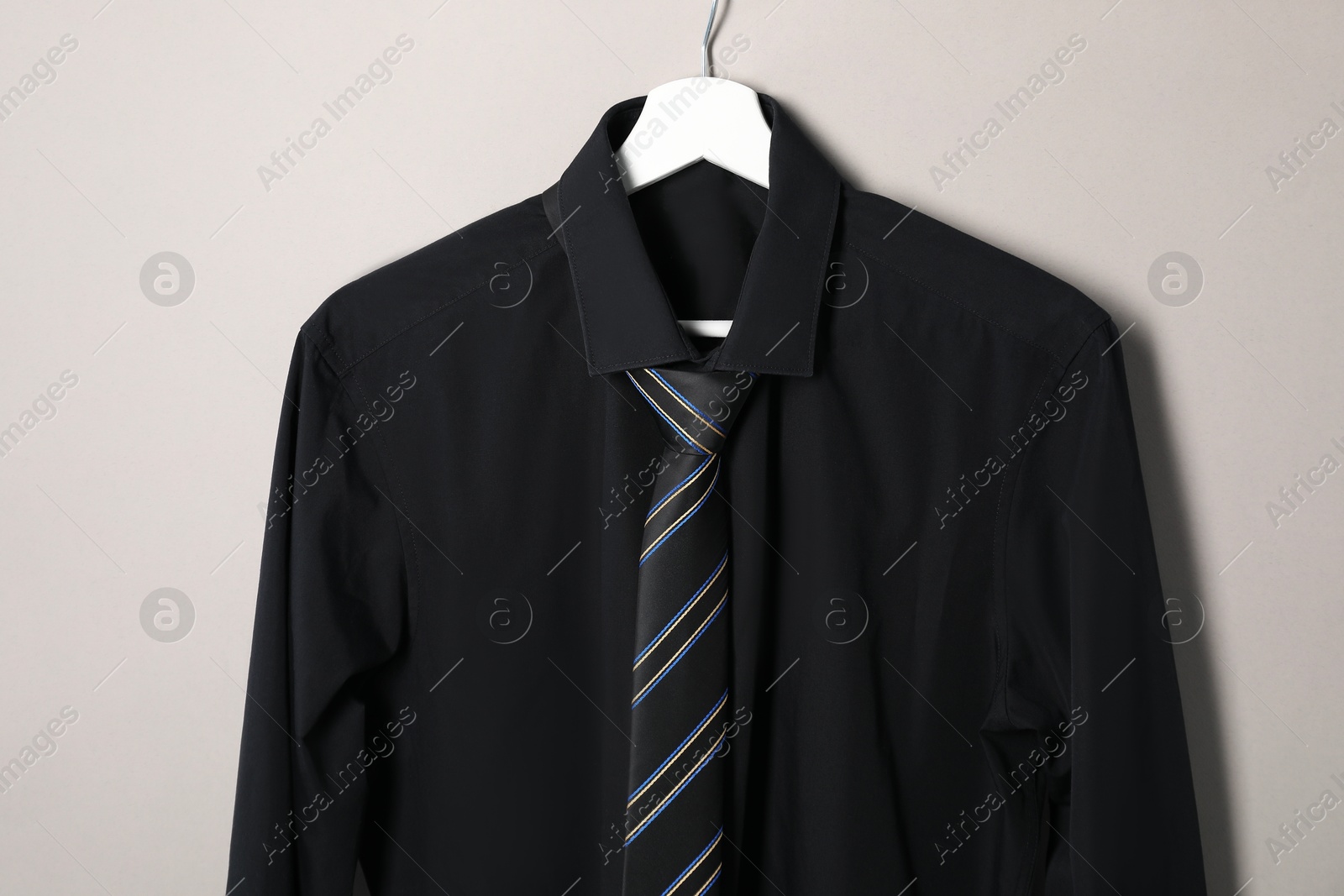 Photo of Hanger with shirt and striped necktie on light background