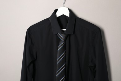 Hanger with shirt and striped necktie on light background