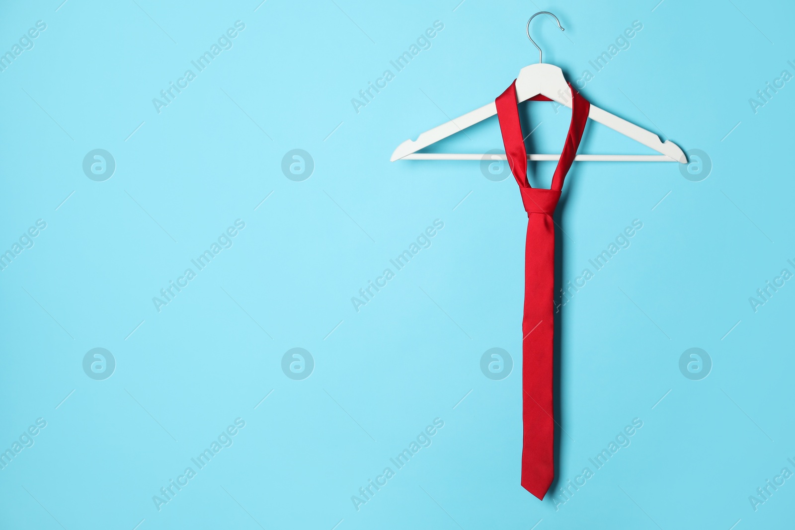 Photo of Hanger with red tie on light blue background. Space for text