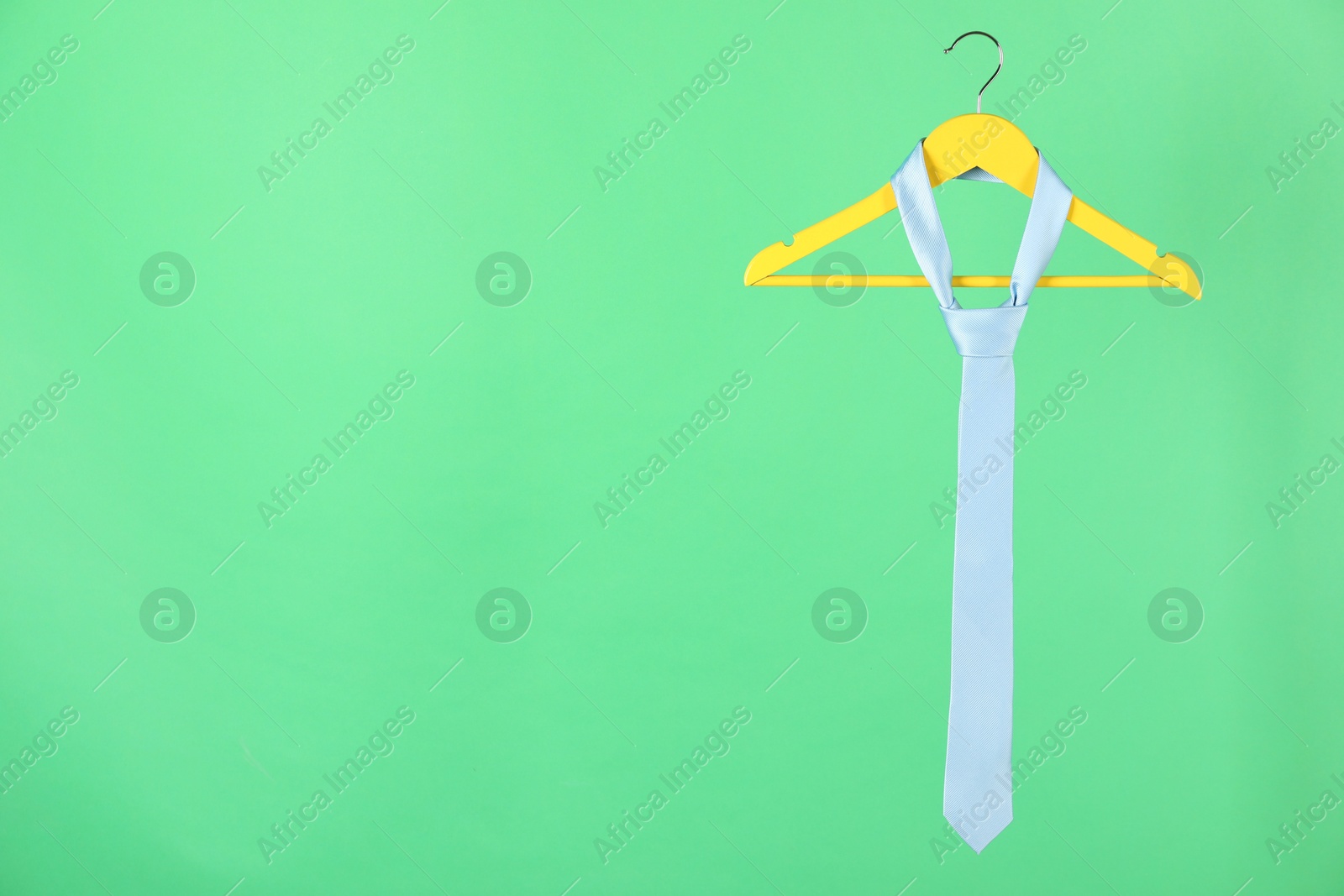 Photo of Hanger with light blue tie on green background. Space for text