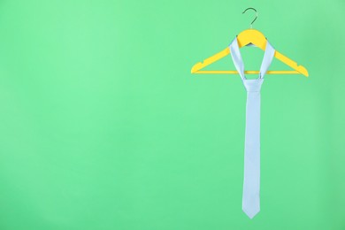 Photo of Hanger with light blue tie on green background. Space for text