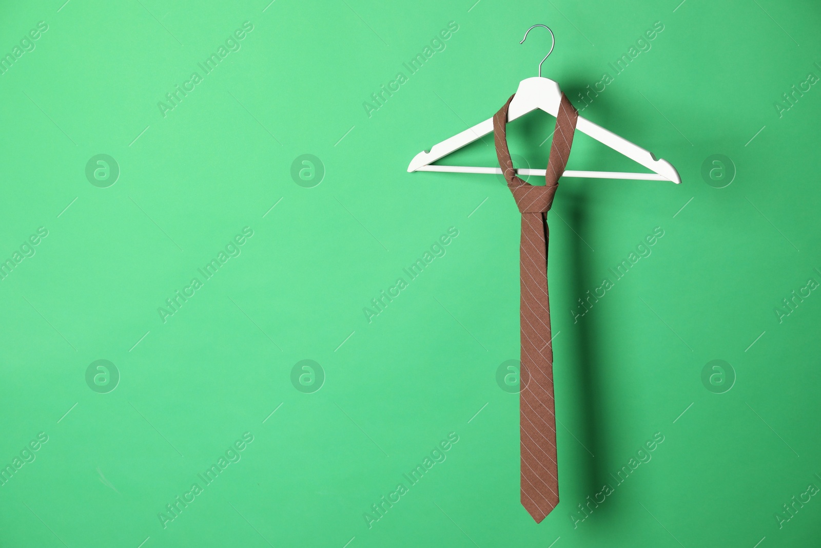 Photo of Hanger with brown striped tie on green background. Space for text